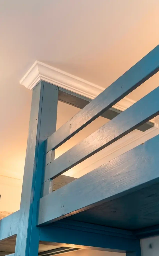 a vertical realistic shot looking up at the top bunk safety rail, painted dusty blue, with a white ceiling filled
