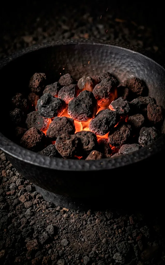 Close-up of a black fire bowl with glowing embers and lava rocks.