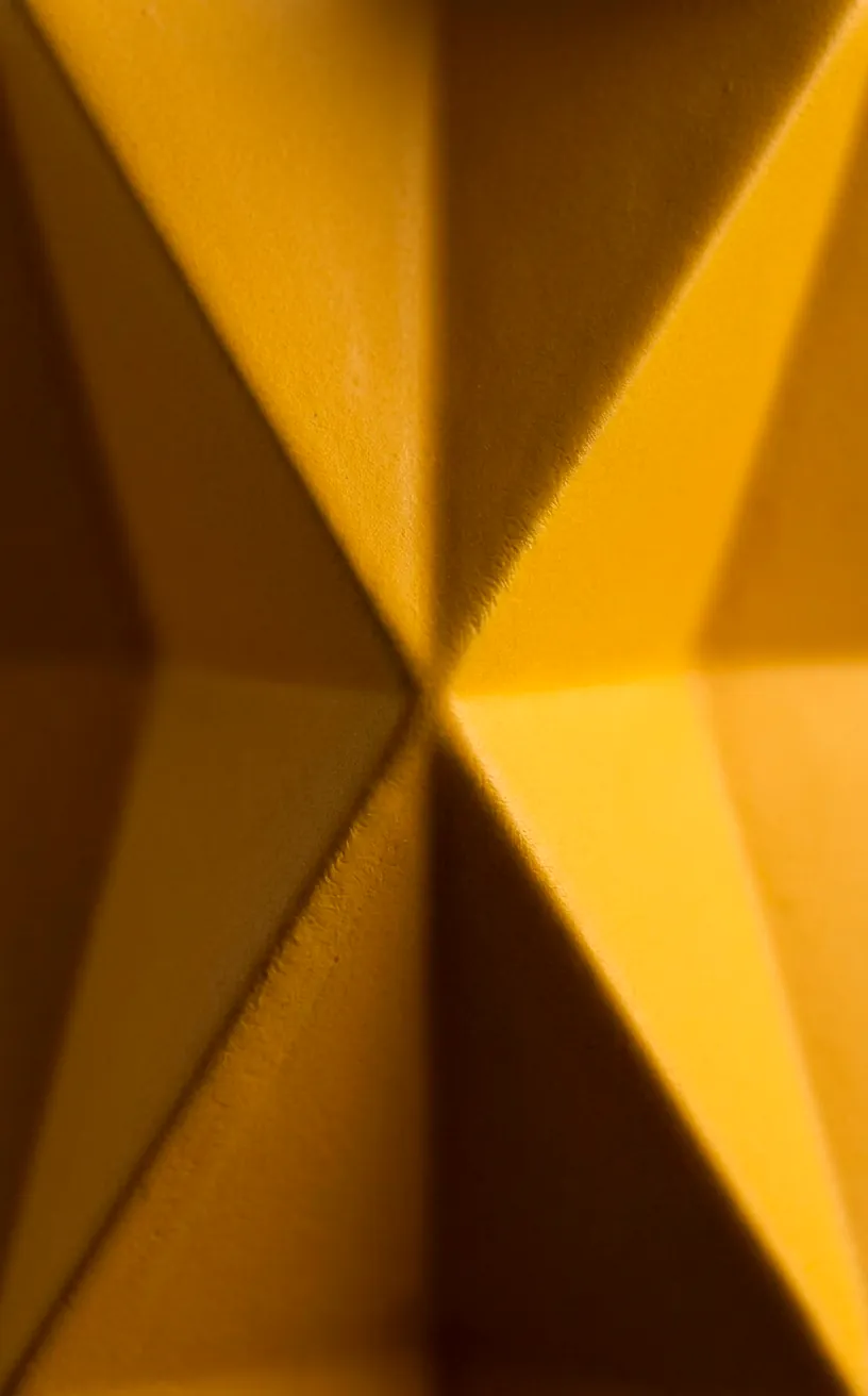 Close-up of the sharp, faceted planes of a geometric yellow planter.