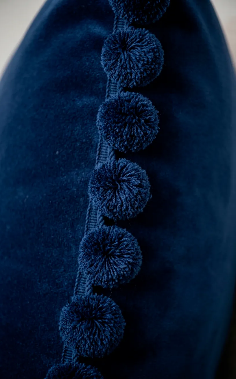 Detail of navy blue pom-pom border on a soft velvet throw pillow.