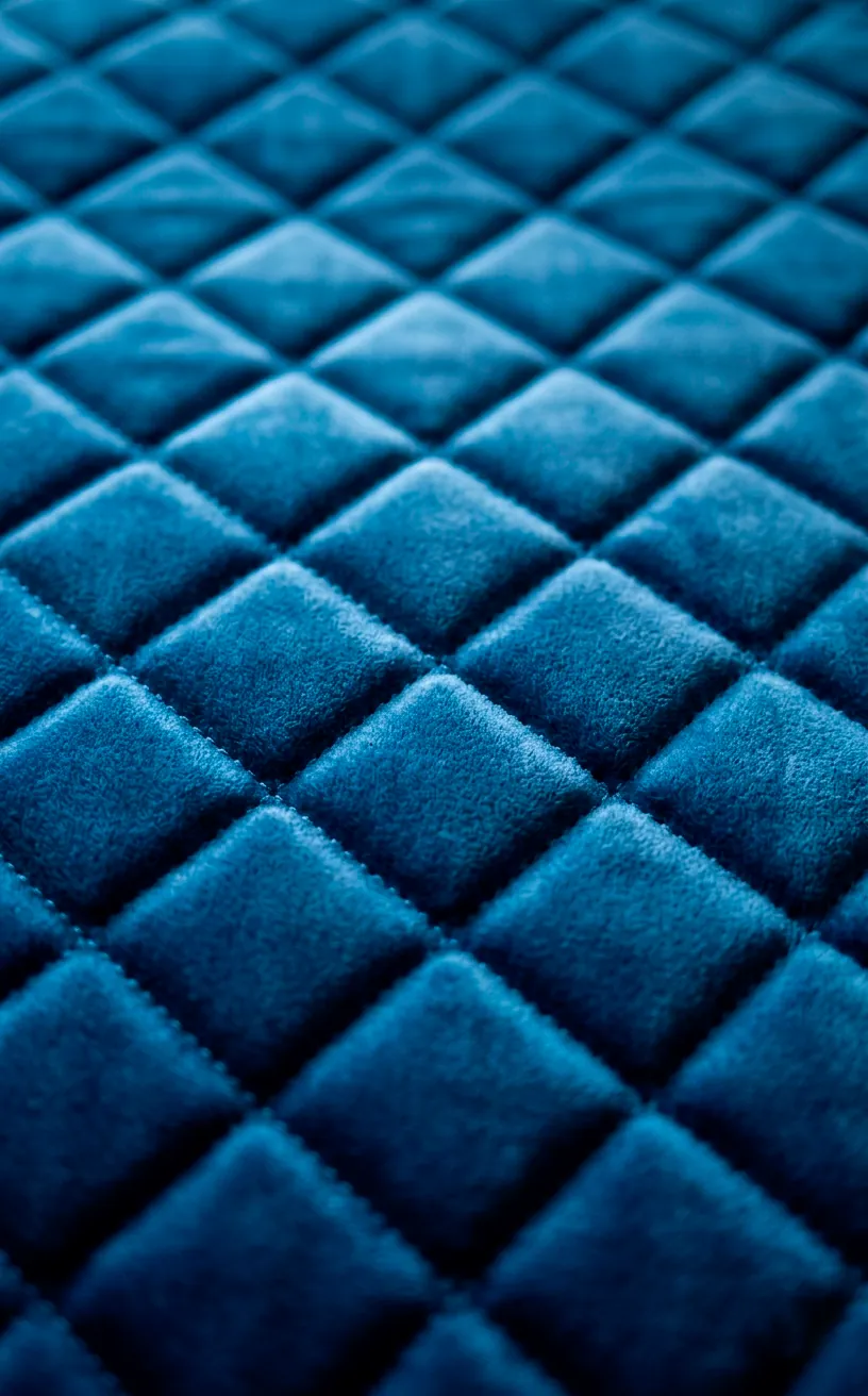 Close-up of diamond-quilted velvet fabric in a rich mustard yellow.