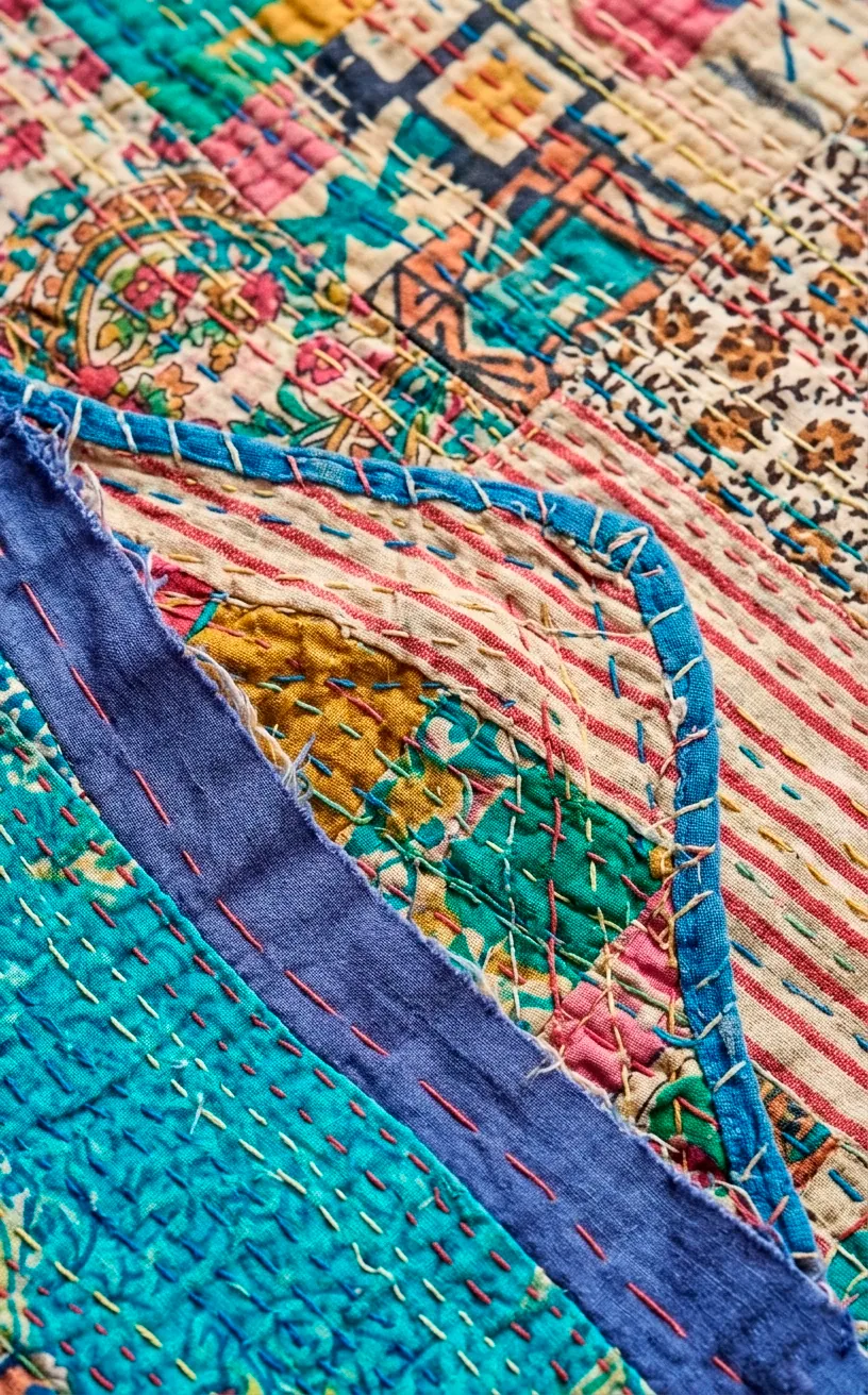 Close-up of hand-stitched details and layered fabrics on a colorful Kantha quilt.