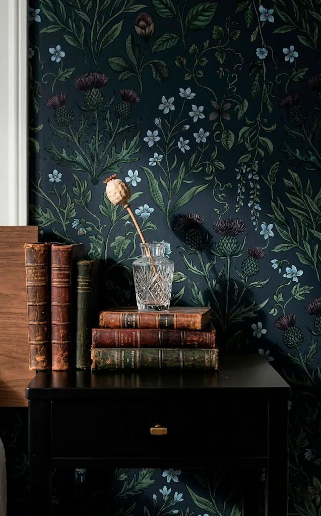 Detail shot of moody floral wallpaper behind a black nightstand with vintage books.