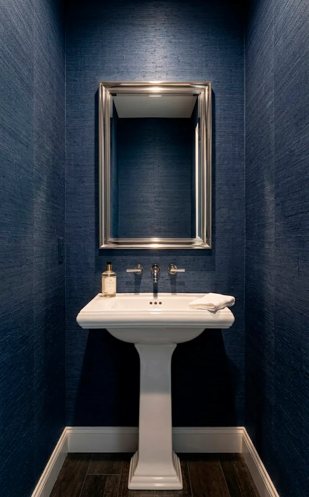 Navy blue grasscloth wallpaper in a powder room with silver accents and organic texture.