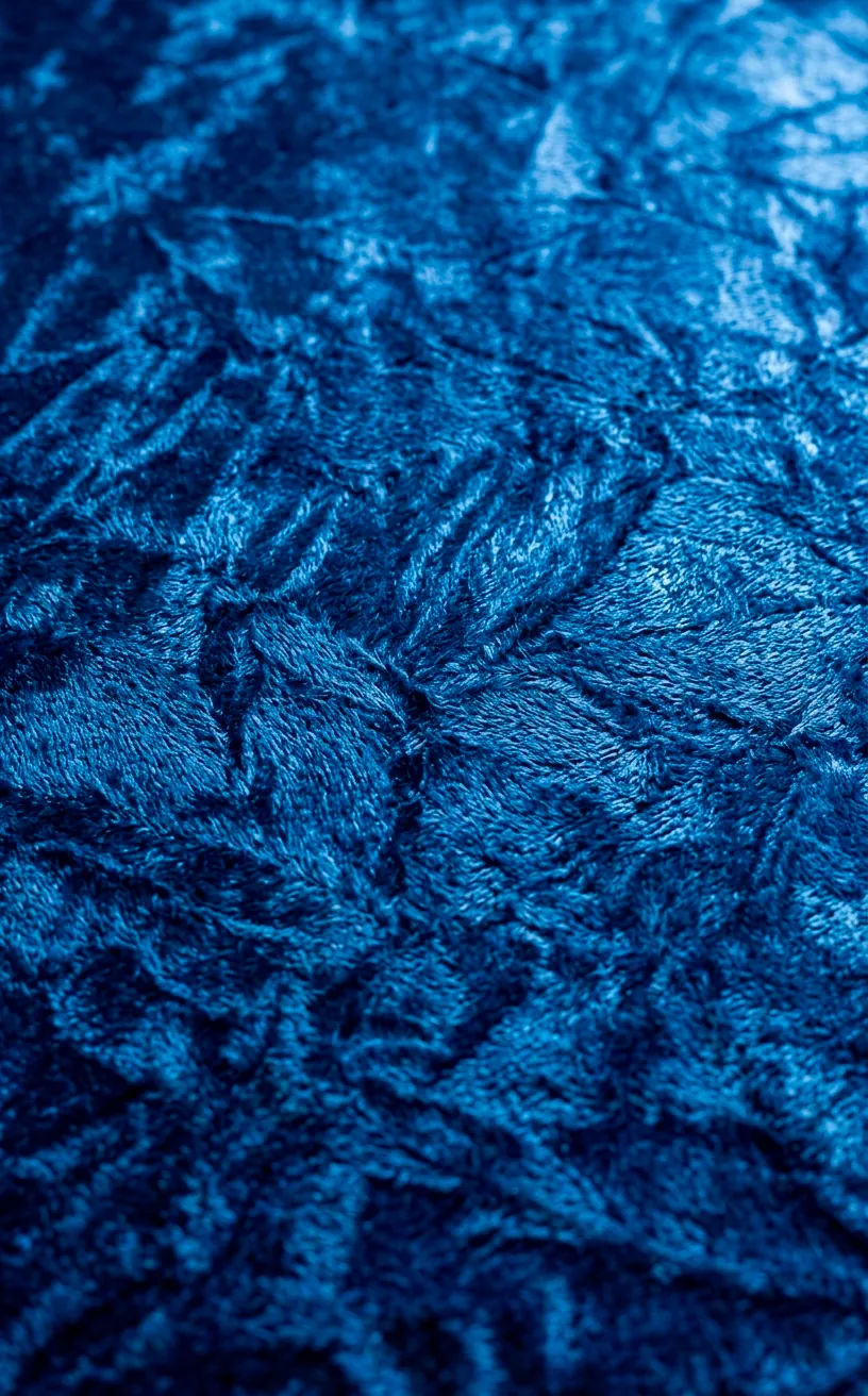 Macro detail of crushed navy blue velvet fabric highlighting its unique reflective sheen.