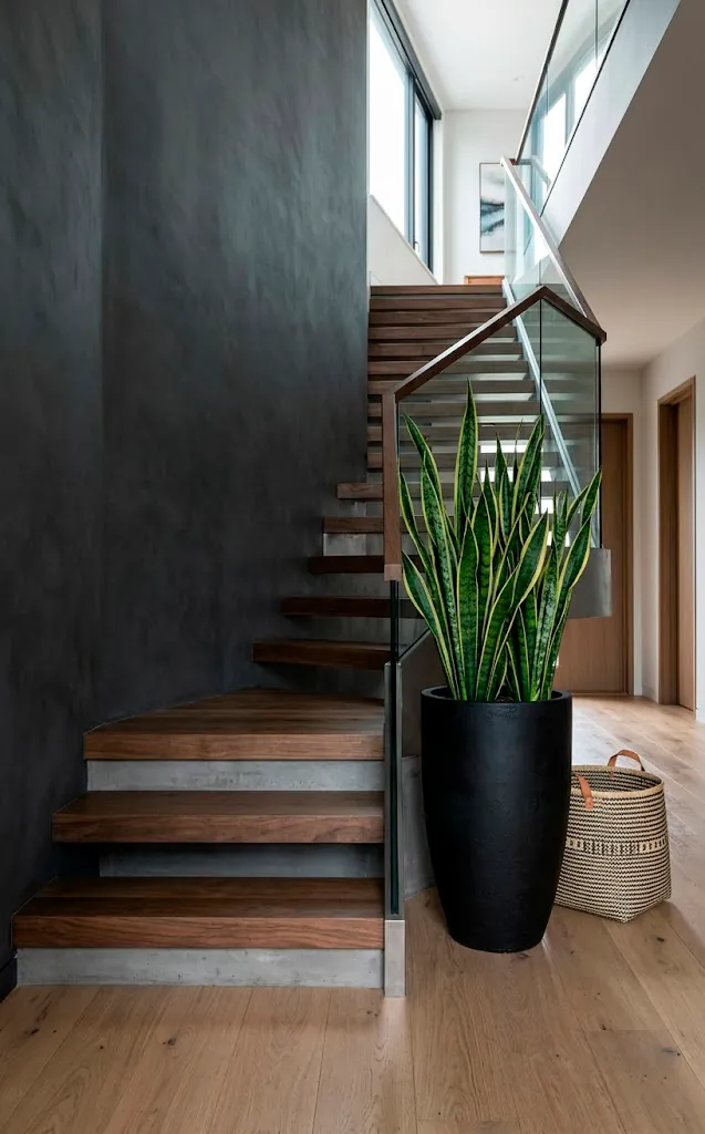 Base of a modern minimalist staircase featuring a tall snake plant in a black ceramic planter and a woven basket.