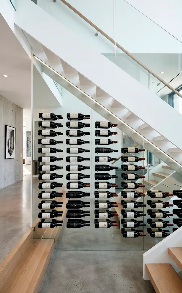 Minimalist wine cellar with floating metal pegs and clear acrylic cradles under stairs