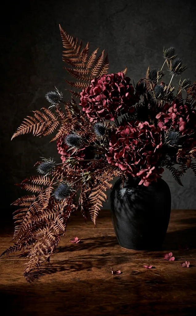 Large centerpiece of dried moody florals and ferns in a black vase.