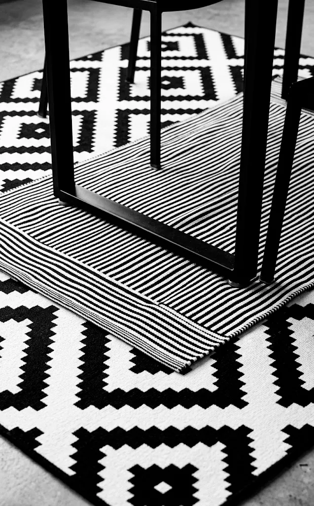 Layered black and white rugs with diamond and stripe patterns under a black table.
