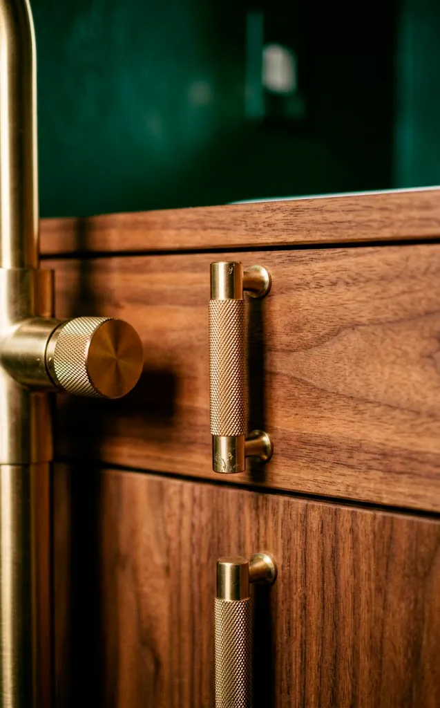 Close-up of a knurled brass faucet and cabinet pulls on a walnut wood bathroom vanity.