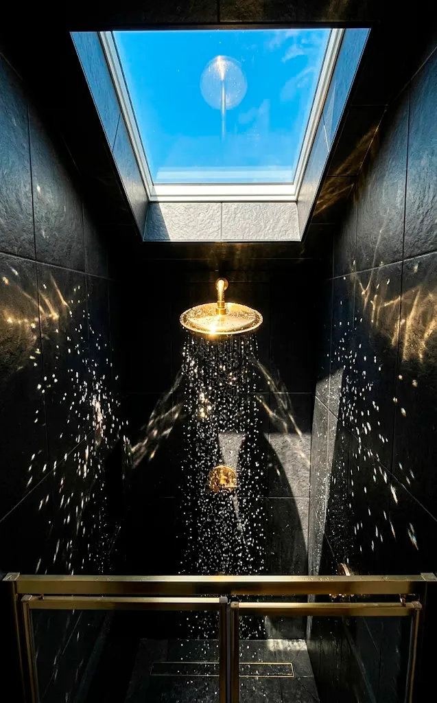Sunlight from an attic skylight reflecting off a gold shower head in a black shower.